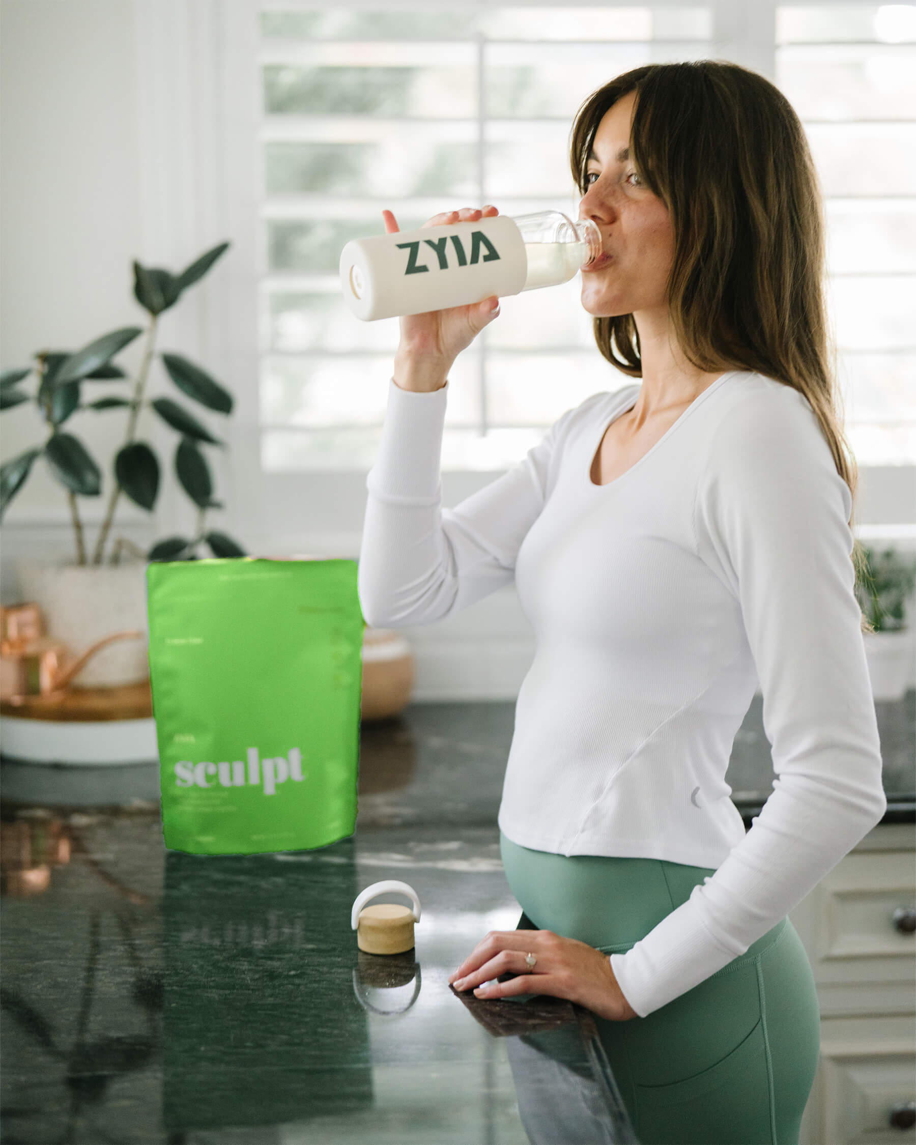 Woman drinking ZYIA Sculpt in her kitchen